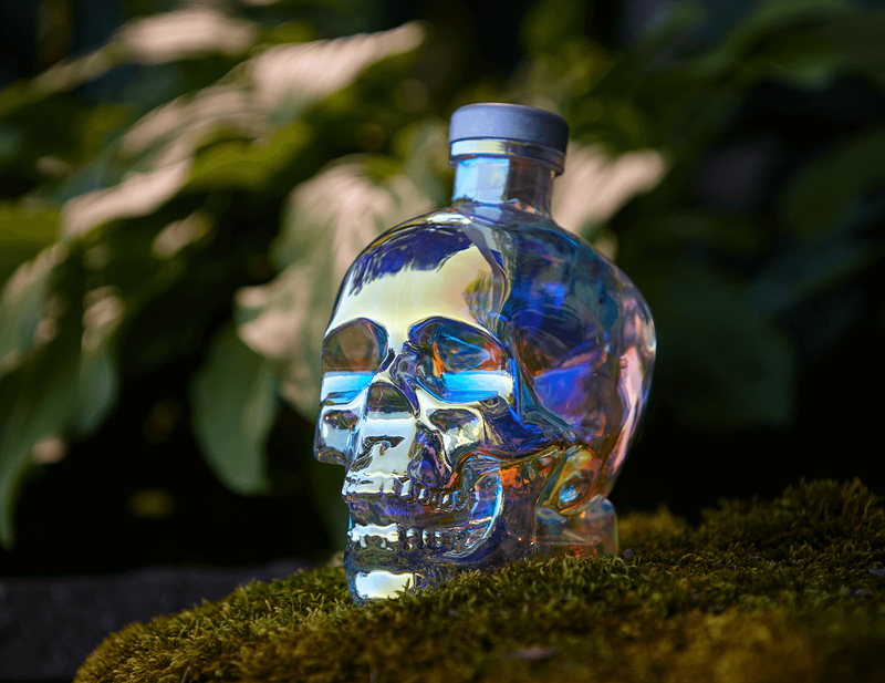 A bottle of Aurora Crystal Head Vodka is displayed on a moss covered rock